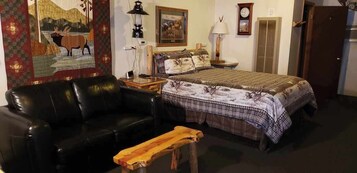 Una habitación con una cama, un sofá de cuero negro, un banco de madera, un reloj de pared y un cuadro.