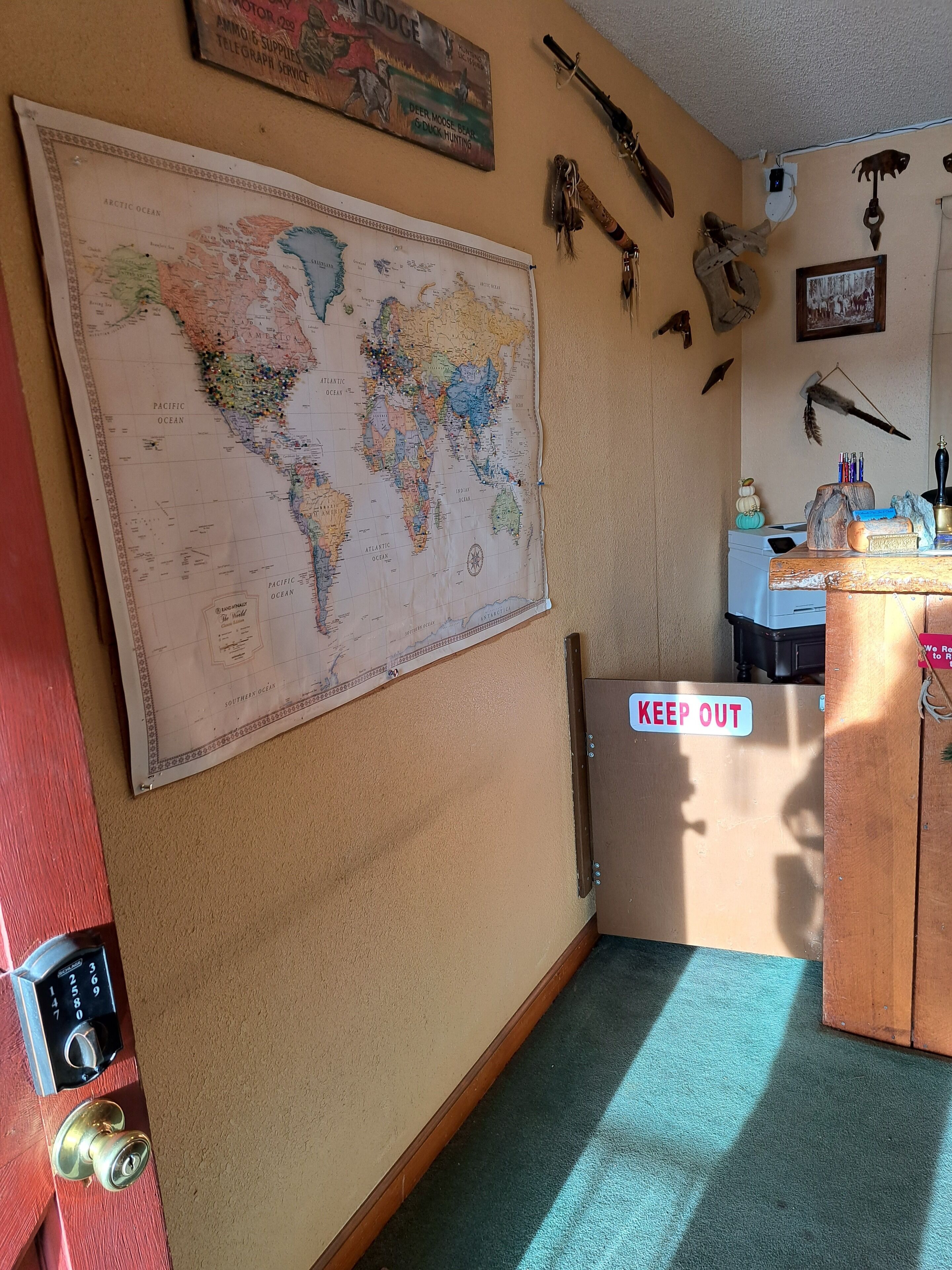 A room with a large world map on the wall, a 'KEEP OUT' sign, and various hunting-related items.