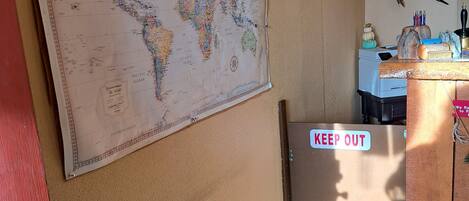 A room with a large world map on the wall, a 'KEEP OUT' sign, and various hunting-related items.