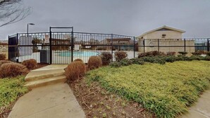 A gated residential area with a swimming pool, a single-story building, and a paved pathway. - Cozy and stylish 4Bedroom 4.5bath Townhome (Lewisville)