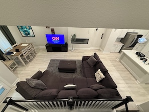 A modern living room with a large sofa, a flat-screen TV, a dining area, and a kitchen. - Cozy and stylish 4Bedroom 4.5bath Townhome (Lewisville)