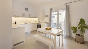 A modern kitchen with white cabinetry, a dining table with a bench, and a potted plant. - Kerameikou25 large · Beautifully curated 1BR (Athens)