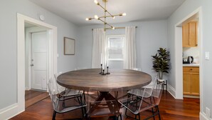 A dining room with a round table, six chairs, a chandelier, and a potted plant.