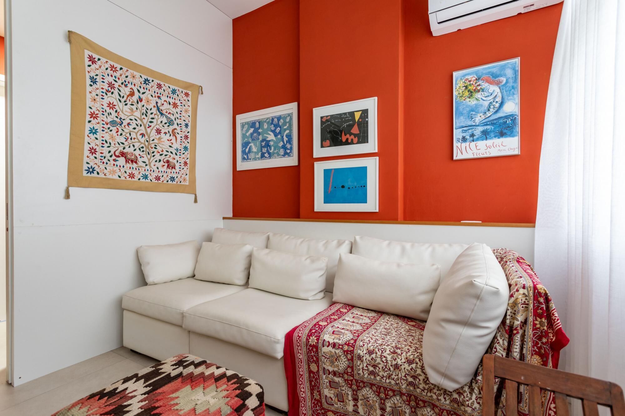 Una sala de estar con un sofá blanco, un tapete estampado y una pared roja con obras de arte enmarcadas.
