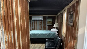 Un couloir étroit mène à une chambre qui contient un lit, un fauteuil en cuir noir et une porte dotée d’un système de verrouillage à clavier.