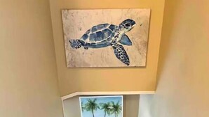 Un escalier en bois menant à un palier où est accrochée une peinture encadrée représentant une tortue et un paysage de plage.