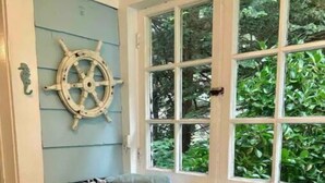 Une salle de bain avec une fenêtre, un décor en forme de barre de timon de navire, un porte-serviettes et un bac de rangement.