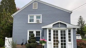 Une maison à deux étages, avec une façade grise, des boiseries blanches et un petit porche doté d’une porte et de fenêtres blanches.