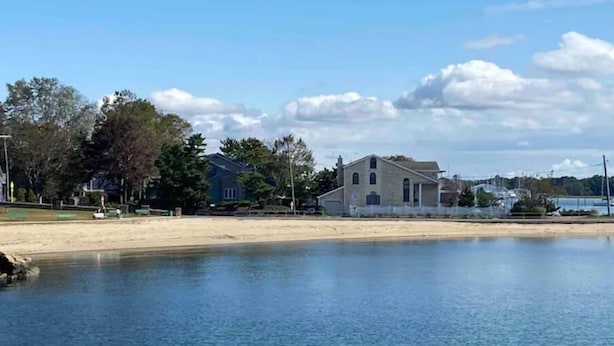 Il s'agit d'une propriété située au bord de l'eau, avec une plage de sable et un lac paisible. On peut y apercevoir deux maisons : l'une a un toit à pignon et l'autre, un toit plat.