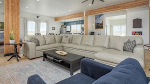 A spacious living room with a large L-shaped sectional sofa, a dark coffee table, and a wooden accent wall. - Newly renovated Barnhouse on 13 acres brings you a modern feel to your retreat.  (Grand Junction)
