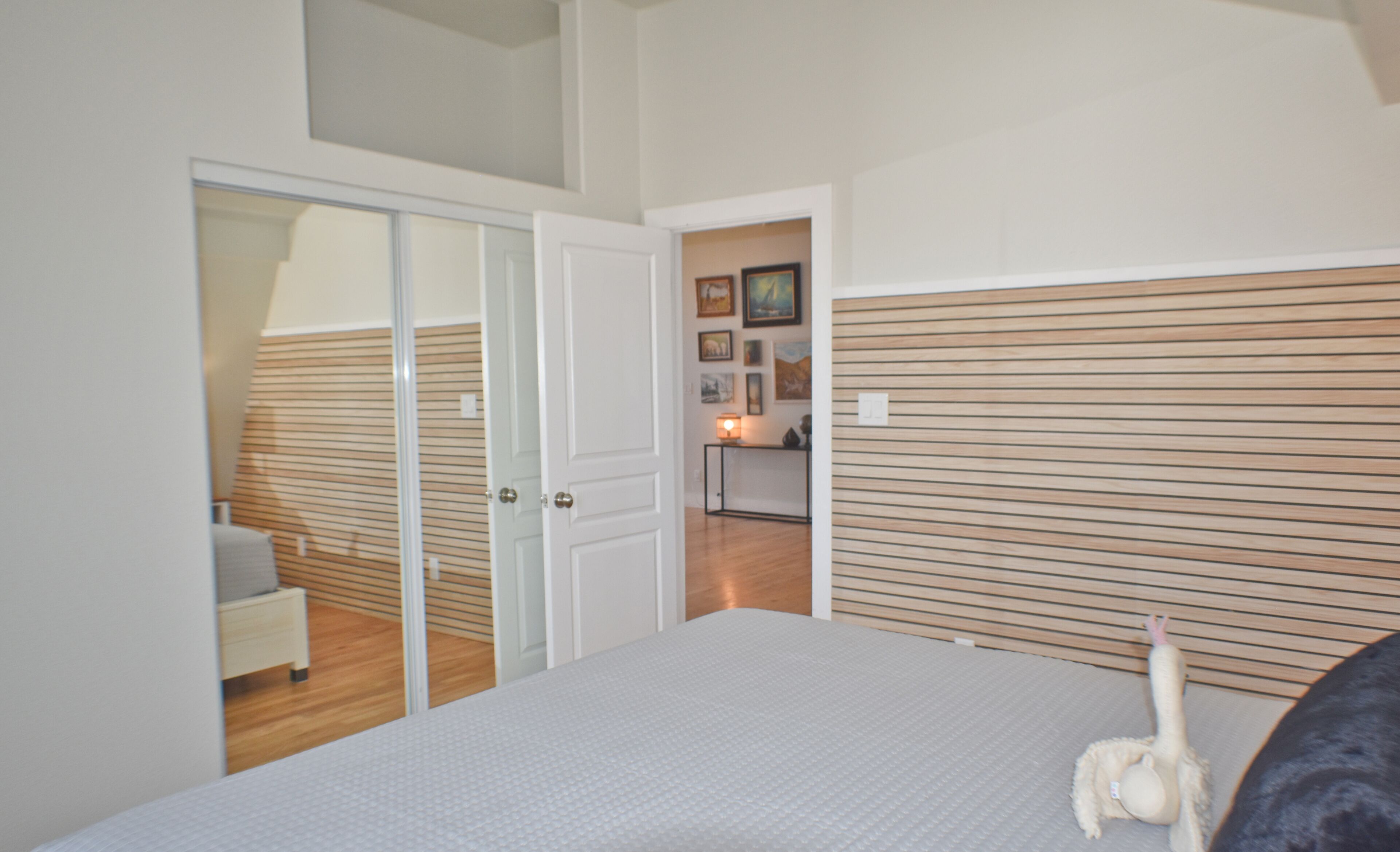 A bedroom with a bed, a wardrobe, a bedside table, and a wall with framed pictures.