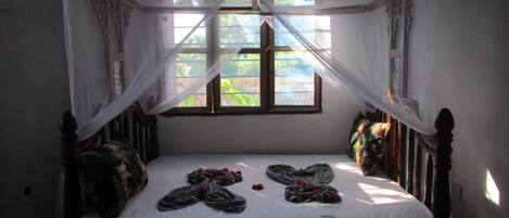 A bed with a canopy, a window, and a view of greenery outside.