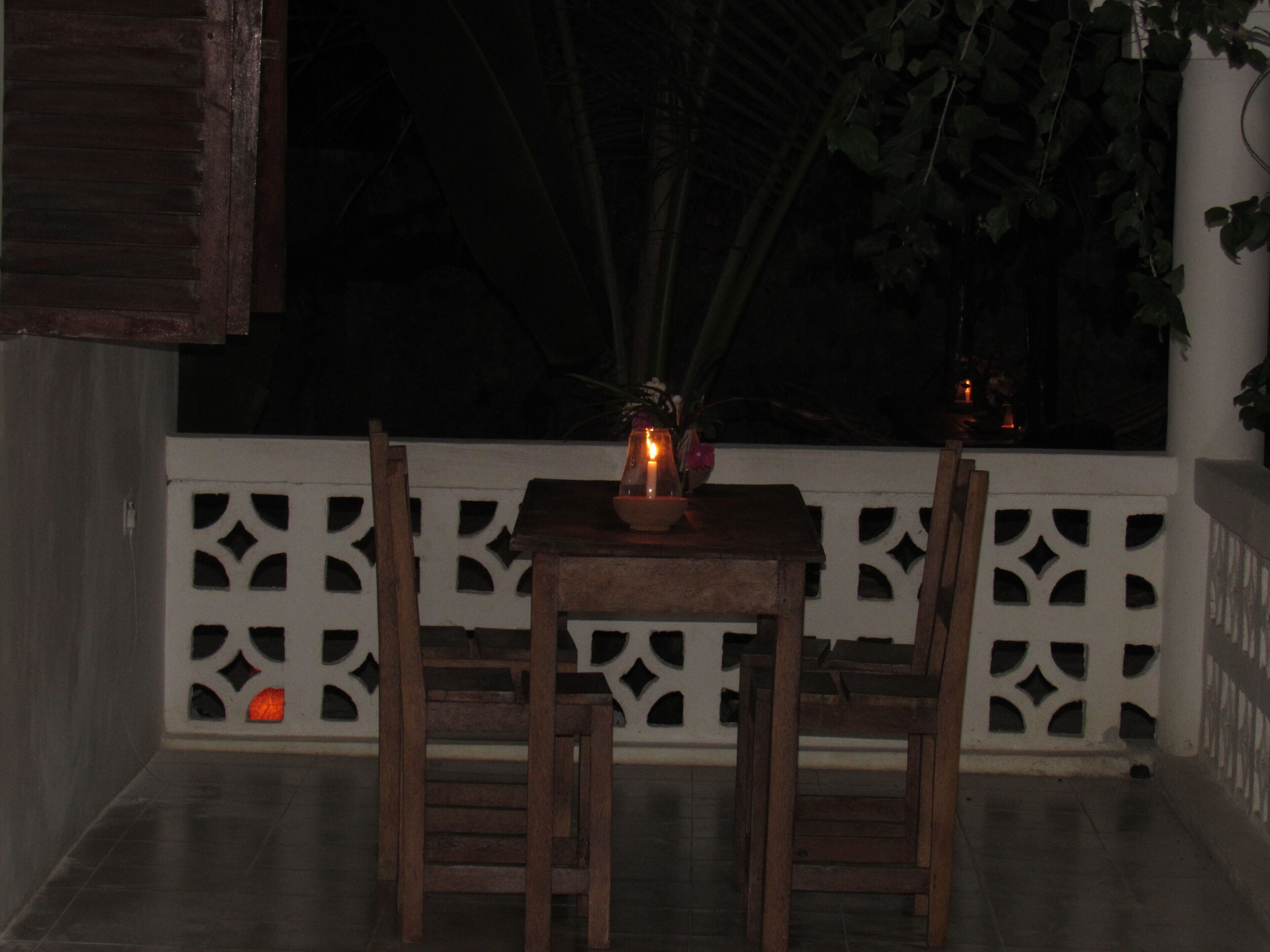 Mesa de madeira com cadeiras numa varanda, uma vela e uma janela com vista para o céu noturno.