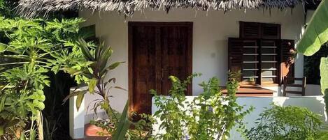 A small house with a thatched roof, surrounded by lush greenery and palm trees.