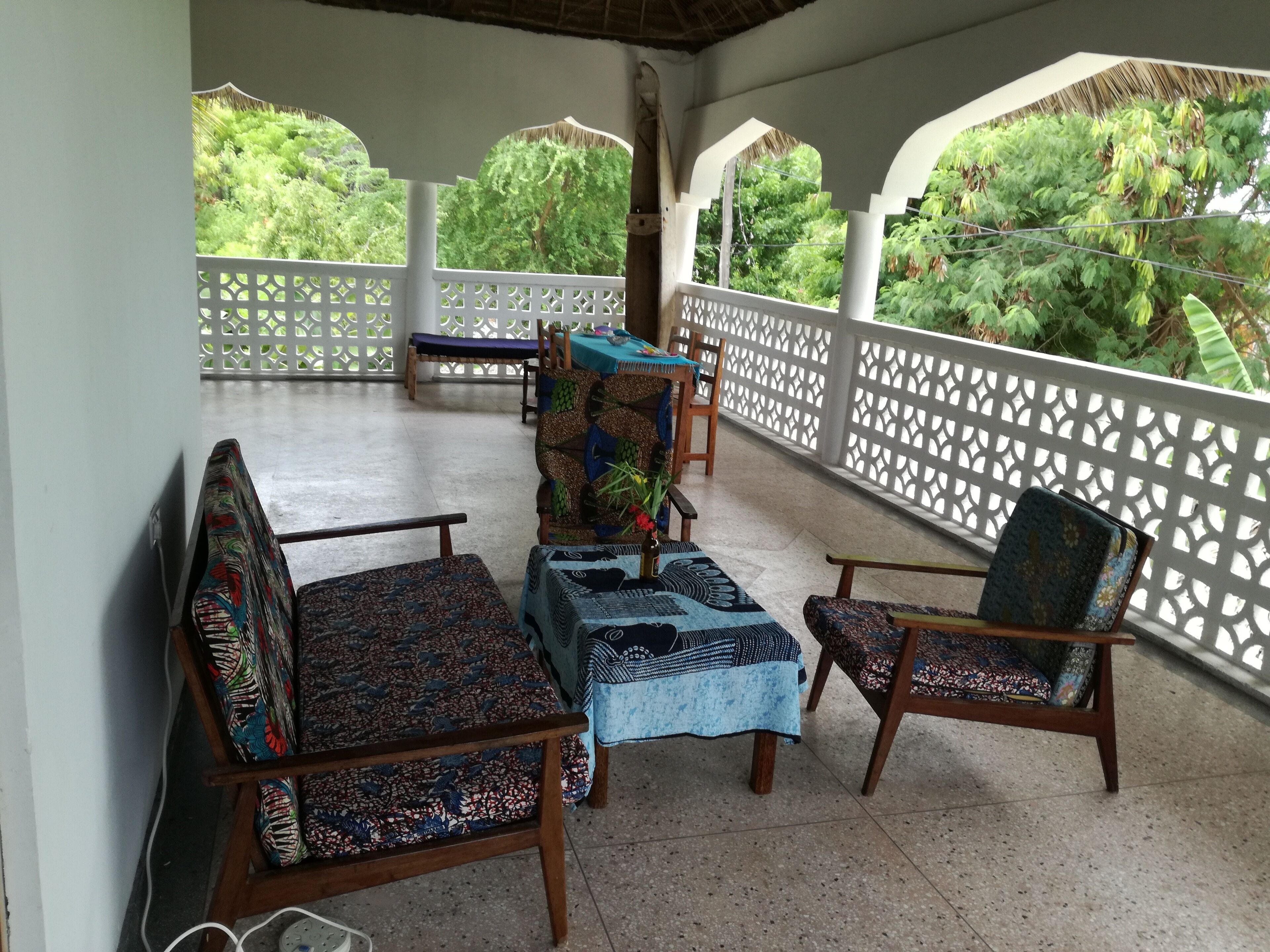 Un espace extérieur aménagé, abrité et doté de mobilier aux motifs originaux, offrant une vue sur une végétation luxuriante.