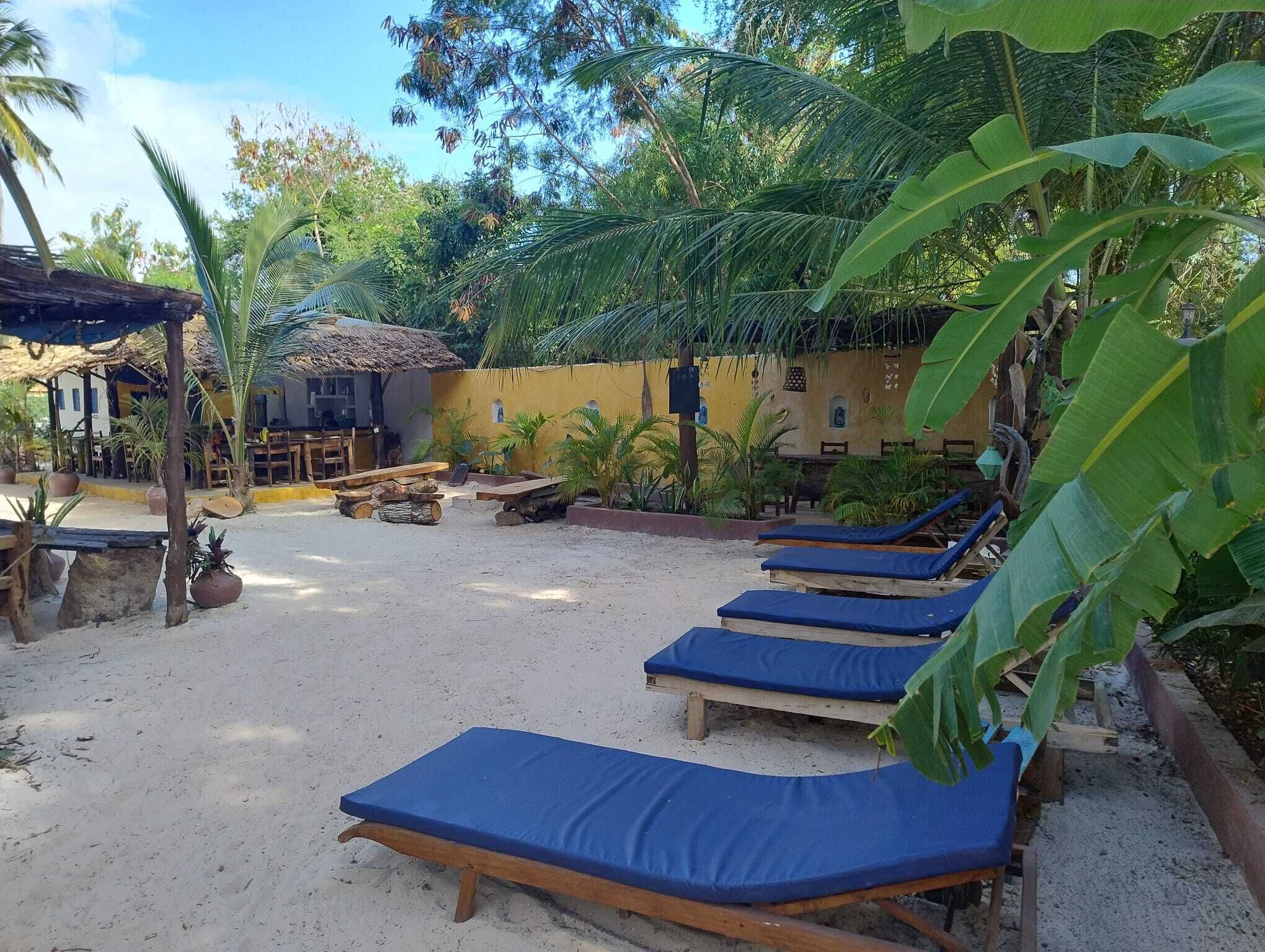 A beachside resort with sun loungers, a thatched-roof hut, and lush greenery.