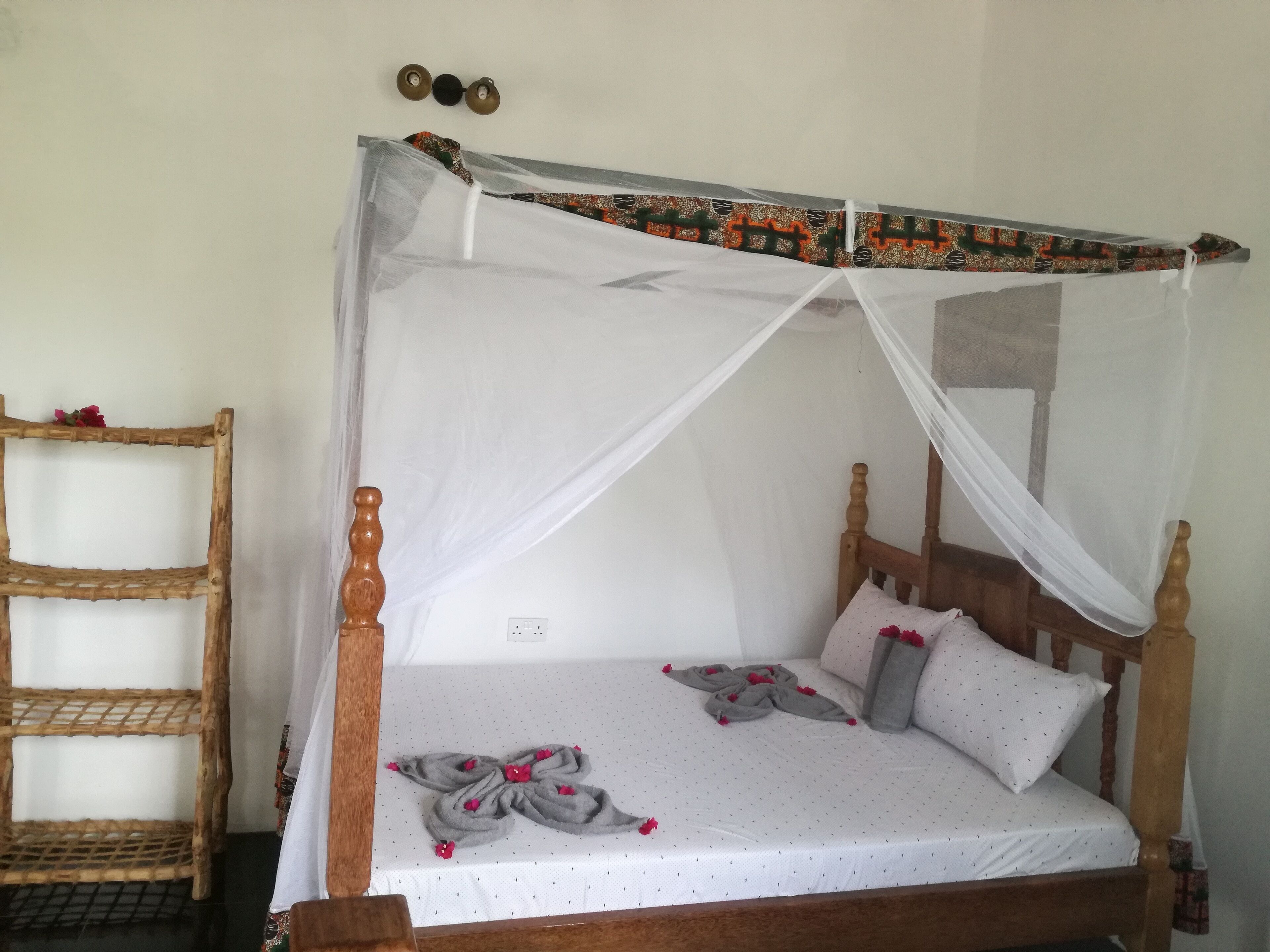 A bed with a white canopy, a wooden headboard, and a grey bedspread with red flowers.