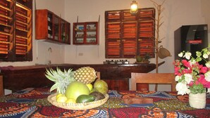 Uma sala de jantar com uma mesa posta para refeição, com uma cesta de frutas e um vaso de flores.