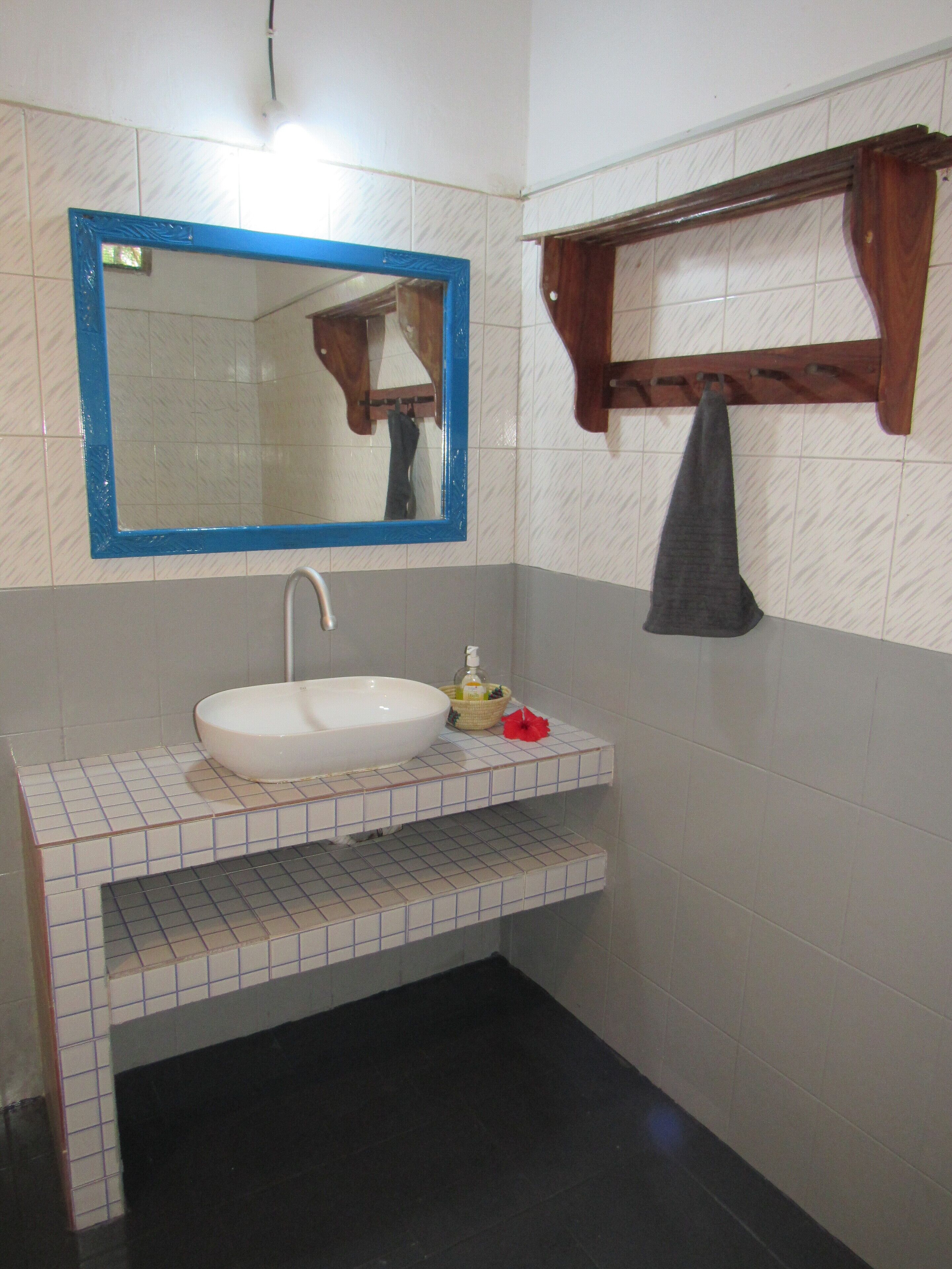 A bathroom with a white sink, a blue-framed mirror, a wooden towel rack, and a tiled floor.