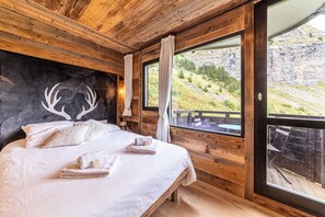 Ein Schlafzimmer einer Holzhütte mit einem Bett, einem Hirschgeweih als Wanddeko und einem Balkon mit Bergblick.
