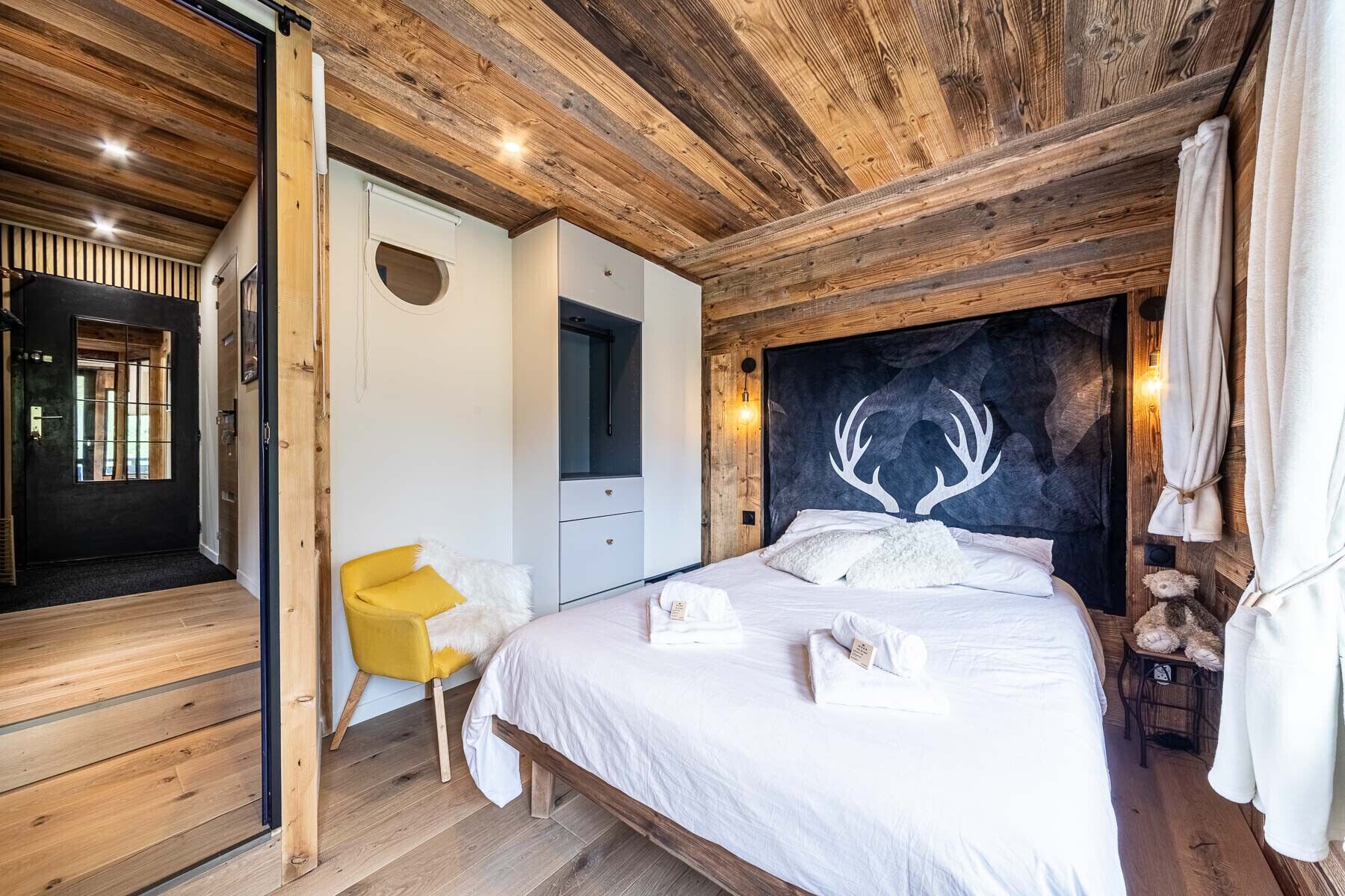 Ein Schlafzimmer einer Holzhütte mit Bett, Stuhl und einem Kopfende im Geweih-Design.