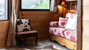 A cozy room with a wooden cabin interior, featuring a leather chair, a bed with patterned bedding, and a window with curtains. - Immodreams - La Grange - Avoriaz (Avoriaz)
