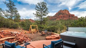 An outdoor patio with a hot tub, seating area, and a swing set, surrounded by red rock formations and trees. - Red Rock Bonanza +Hot Tub, Hikes & Views! (Sedona)