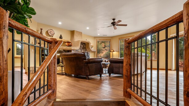A wooden staircase with a metal railing leading to a living area with leather chairs, a fireplace, and a ceiling fan. - Red Rock Bonanza +Hot Tub, Hikes & Views! (Sedona)