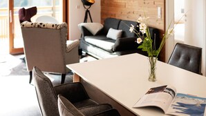 Una sala de estar moderna con una mesa blanca, un sofá negro y un sillón de mimbre. Hay un jarrón con flores sobre la mesa y una lámpara en la esquina.