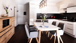 Una cocina moderna con armarios blancos, encimera negra y un comedor con mesa blanca y sillas grises.
