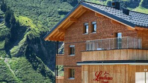 Una cabaña de montaña con fachada de madera y un balcón con vistas a un valle exuberante.