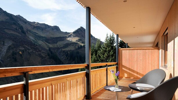 Una terraza de madera con vistas a las montañas, una mesa con sillas y un jarrón con flores.