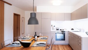 Une cuisine moderne avec une table à manger en bois pour quatre personnes, un four encastré et un grand luminaire suspendu noir.