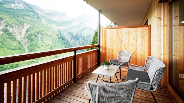 Une terrasse en bois avec une table et des chaises, offrant une vue sur un paysage montagneux.