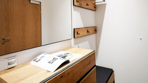 Une chambre avec une commode en bois, un miroir et une étagère en bois dotée de crochets.