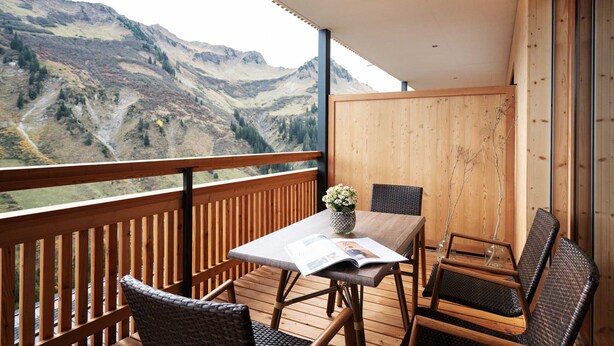 A balcony with a wooden railing, a table with chairs, and a view of mountains. - Landhaus Damüls - mountain view #08 (Damüls)