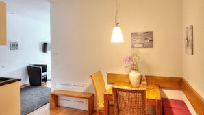 A dining area with a wooden table, wicker chairs, a vase with flowers, and a hanging light fixture.