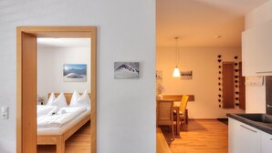 A modern hotel room with a wooden bed, a dining area with a table and chairs, and a kitchen with a sink and cabinets.