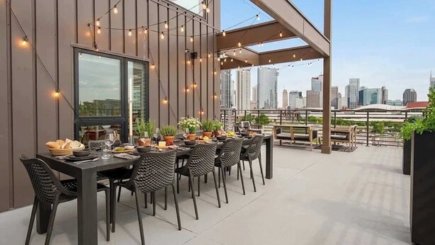 An outdoor dining area with a city skyline view, string lights, and modern furniture. - Dreamy Penthouse | Skyline Views| Largest Balcony! (Nashville)