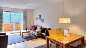 A modern living room with a sofa, a dining table, and a balcony with curtains. - Hölderle Damüls  - mountain view #11 (Damüls)