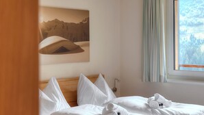A neatly made bed with white linens and pillows, a wooden headboard, and a painting of mountains on the wall. - Hölderle Damüls  - mountain view #11 (Damüls)