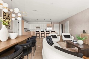 Una sala de estar moderna con sofá, sillas, una mesa de comedor y una cocina al fondo.