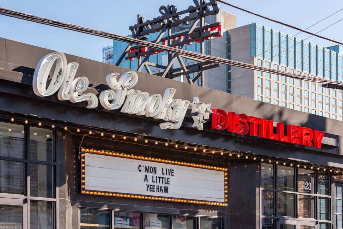 A building with a sign that reads 'Ole Smoky Distillery' and a marquee advertising 'C'MON LIVE A LITTLE YEEHAW'.