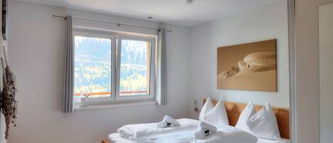 Un dormitorio con cama de madera, ropa de cama blanca, una ventana con cortinas y un cuadro en la pared.