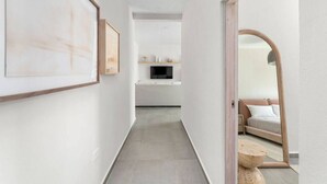 Un pasillo estrecho con una zona de cocina al fondo, una cama con cabecera de madera y un espejo grande a la derecha.