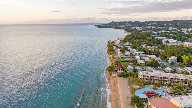 Un pueblo costero con un hotel frente a la playa que cuenta con varias edificaciones, una piscina y una playa.