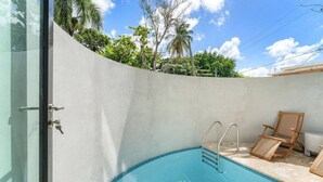 Una piscina con acceso mediante puerta de vidrio, una silla de descanso de madera y un muro de concreto.