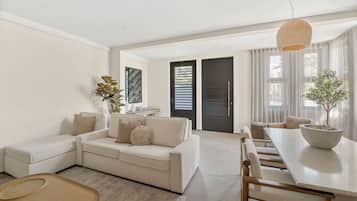 A modern living room with a sofa, dining table, and chairs. There is a door leading to another room.