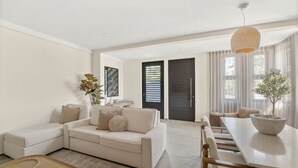 Una sala de estar moderna con sofá, mesa de comedor y sillas. Hay una planta sobre la mesa y un cuadro en la pared.