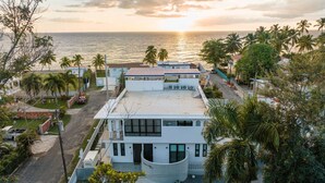 A modern two-story building with a flat roof, surrounded by palm trees and a view of the ocean at sunset. - Casa Loba Luxe Unit 3 w/private pool and garden (Rincon)